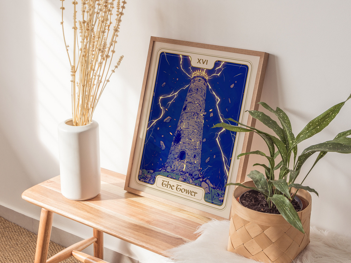 A framed art print titled The Tower features a tall, stone tower surrounded by dramatic lightning against a deep blue background. The artwork is displayed on a wooden table alongside a potted plant and a white vase with dried flowers.
