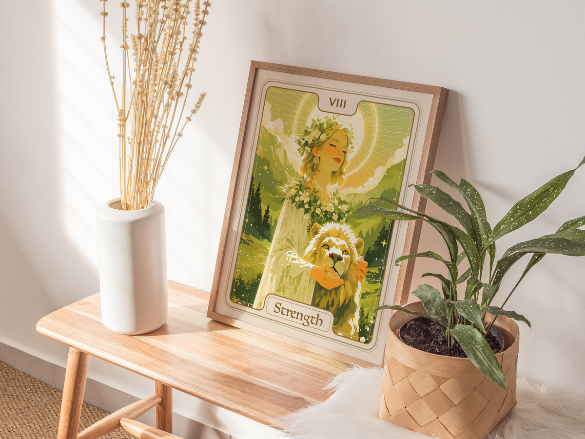 A framed illustration titled Strength features a serene woman adorned with flowers, gently holding a lion. The artwork is set against a lush green background, with soft light illuminating the scene, creating a tranquil atmosphere.