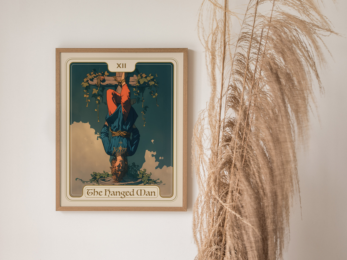 A framed art print of The Hanged Man tarot card, featuring a figure suspended upside down with a serene expression, surrounded by green leaves and a blue sky.