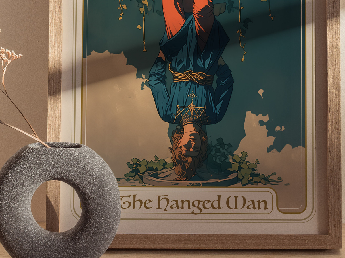 A close-up of a framed art print titled The Hanged Man, depicting a figure hanging upside down surrounded by vines, set against a teal background.
