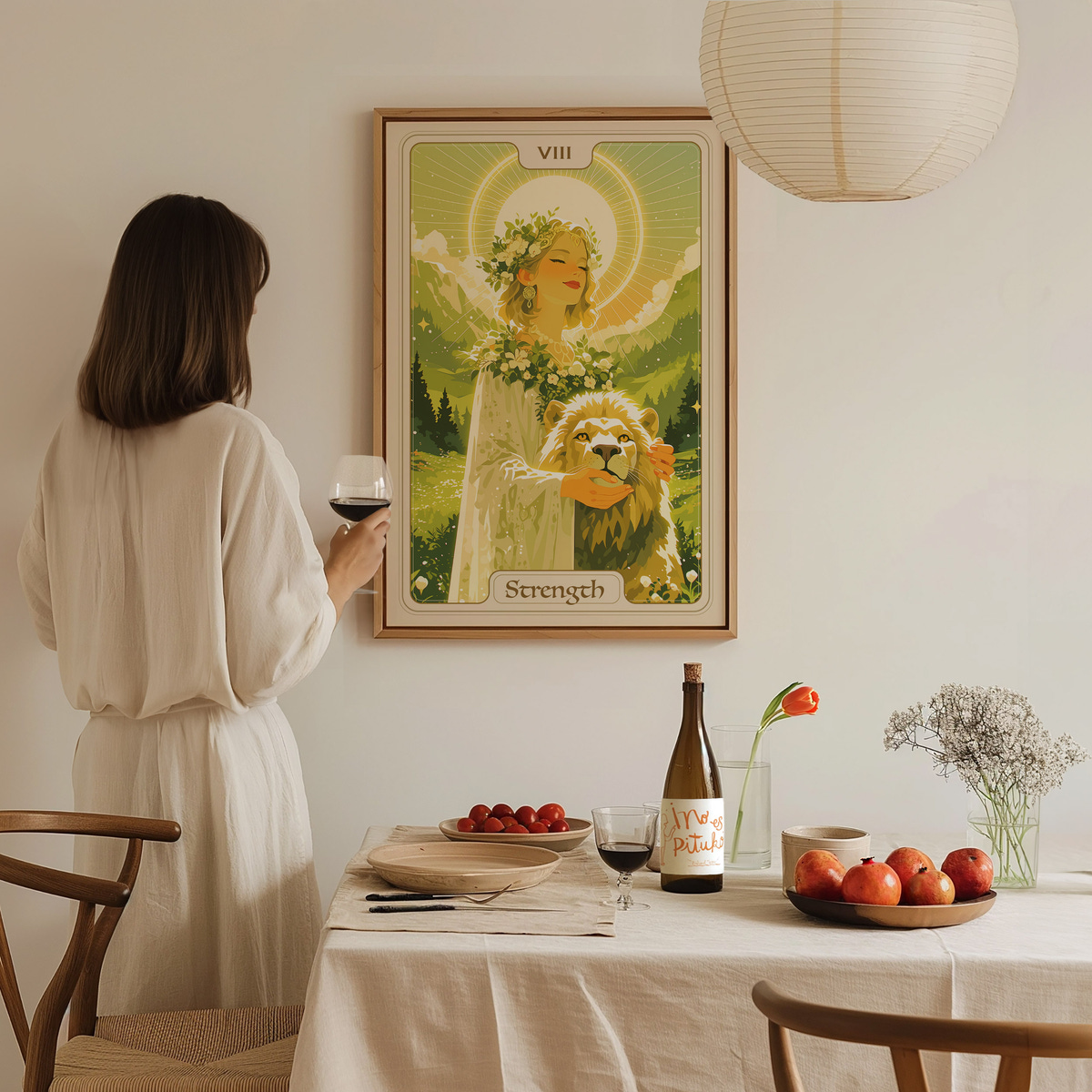 A woman in a white dress stands in a bright, cozy room, holding a glass of wine while admiring a framed artwork depicting a serene figure with a lion.