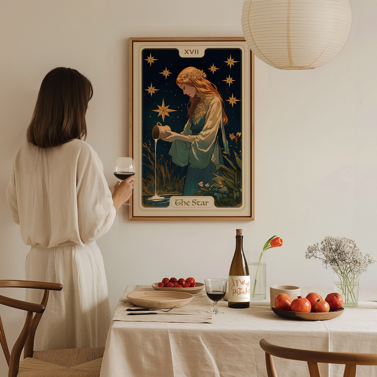 A woman in a light-colored dress stands holding a glass of wine, gazing at a framed tarot card titled The Star on the wall. The dining table, set with apples and a bottle, creates a cozy atmosphere in the softly lit room.