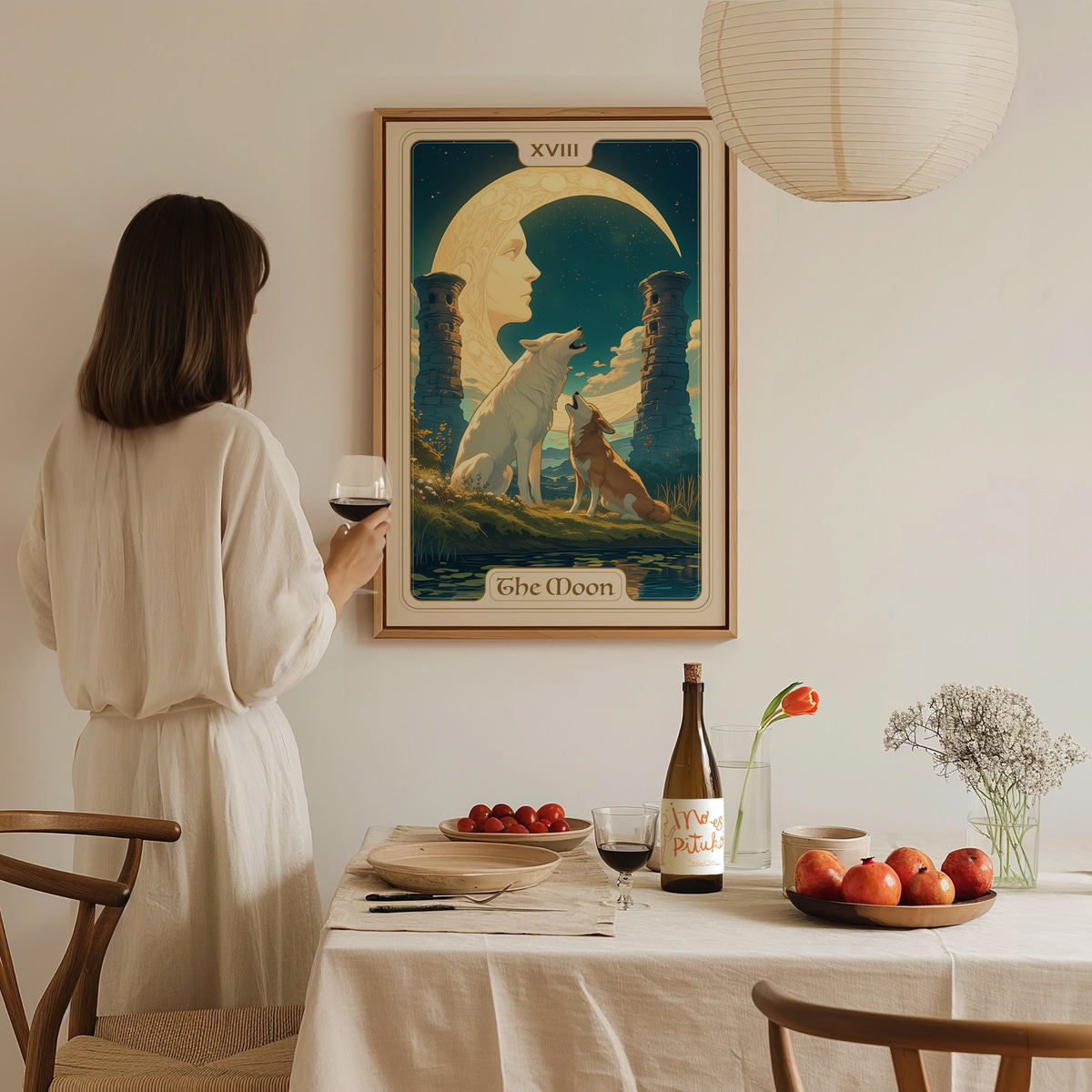 A woman in a light-colored dress stands in a cozy dining area, holding a glass of wine while gazing at a framed art piece titled The Moon.